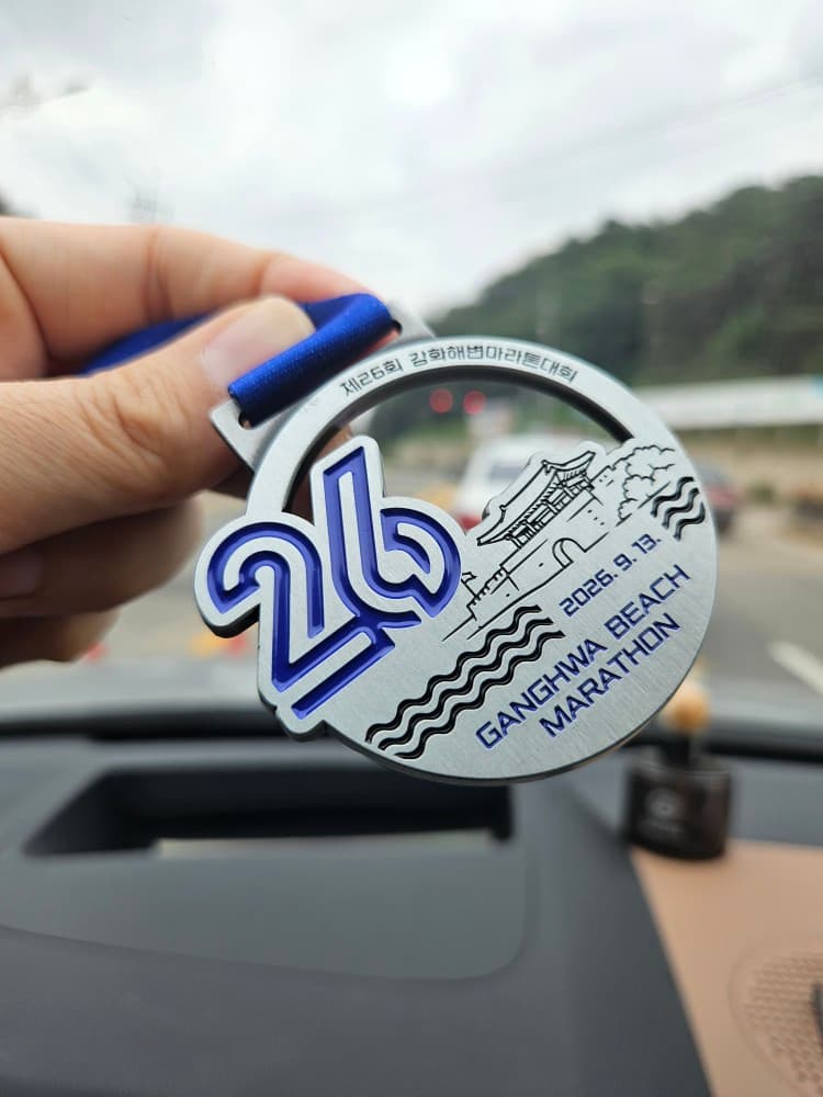 The finisher medal from the 26th Ganghwa Beach Marathon held in one hand